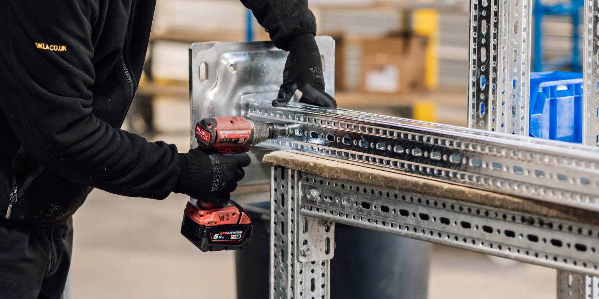 A Sikla steel beam is placed on a table with a person securing a footplate to the beam using a impact drill